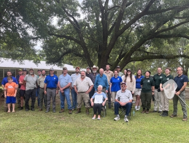 A large group of people pose for a photo outside in front of a large tree.