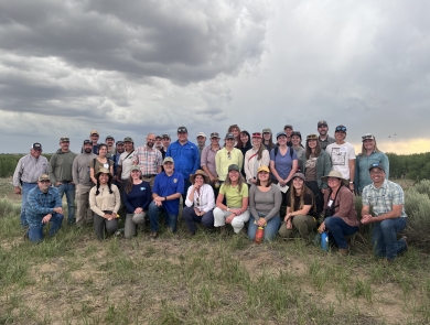 thirty-six people pose for a photo outdoors with a cloudy sky