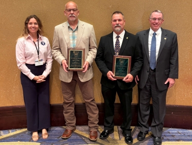 4 people pose; middle 2 with plaques