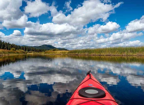 A bright blue sky obstructed by fluffy white clouds reflected off of a stream shot from inside a kayak