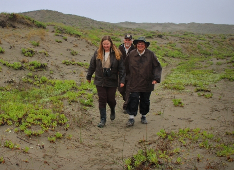 Three people walk on a sand dune