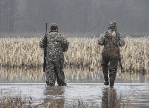 An image of two hunters in camo walking through water.