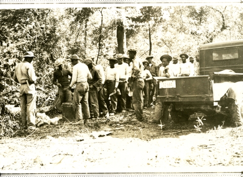 Black and white photo of around 20 African American men in a line in the woods.