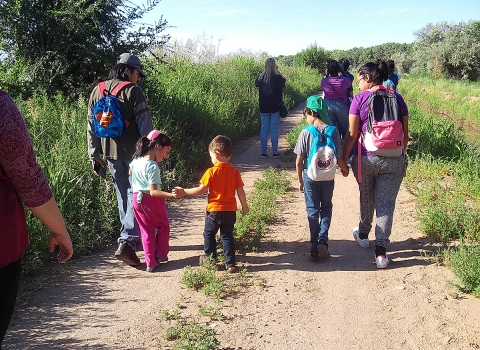 Group of people walking up a grass trail with open ski and high grass on both sides. 