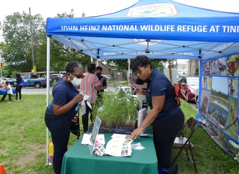 Neighborhood member approaches John Heinz NWR booth as Service staff engages with her.