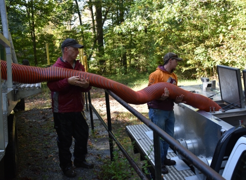 Hatchery personnel transferring trout from truck to truck with stocking hose