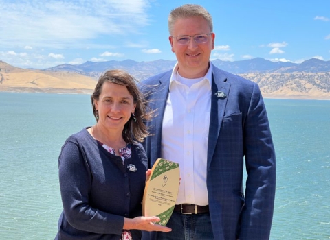 two people stand outside for a photo with a wooden award