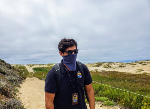 masked person with sunglasses and polo shirt with FWS shield walks through beach like path with native plants