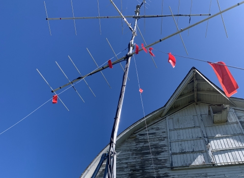 Photo looking up at an antenna array atop a slender pole, with a large old barn in the background.