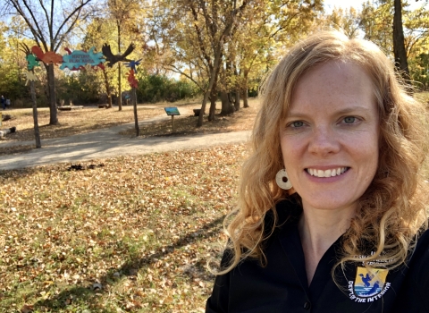 Person with blonde hair takes selfie with fall foliage in the background