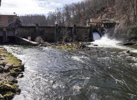 Downstream view of a dam stretching across a river, with water flowing through the right end