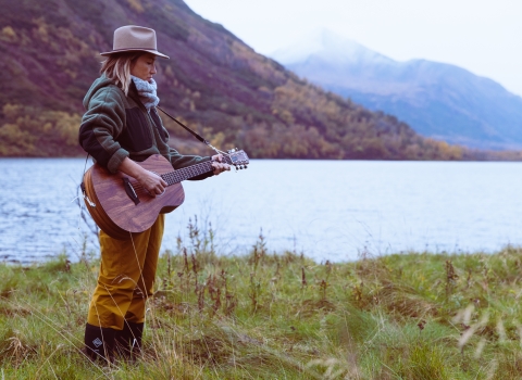 A woman playing guitar next to a lake