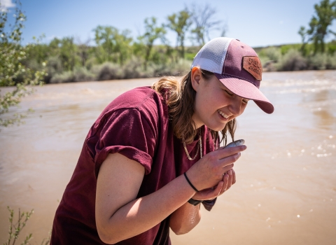 A person smiling while holding a razorback sucker. River in background.