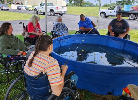 Elderly people fishing out of blue stock tub under a tent