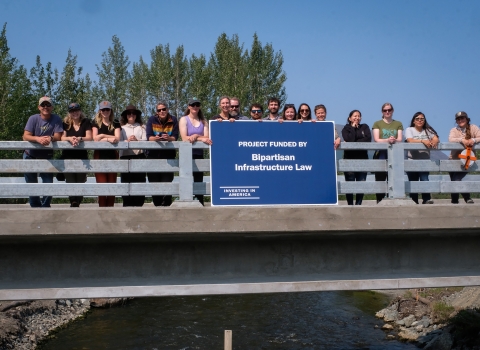 a group of people standing on a bridge over water holding a blue sign