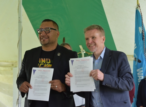 Two men hold up documents for the camera