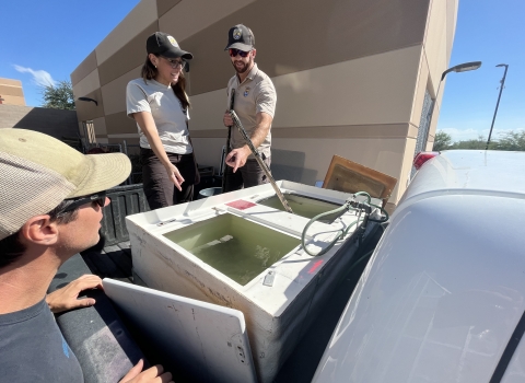 Two Service employees show a teacher the fish tanks in the back of a truck.