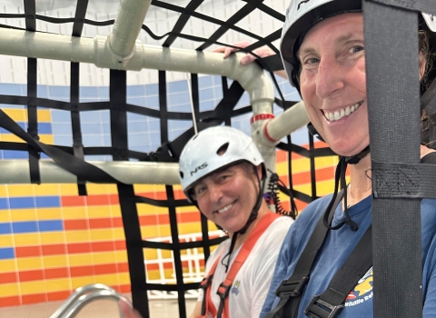 2 people strapped into pvc/harness cage; both wear helmets