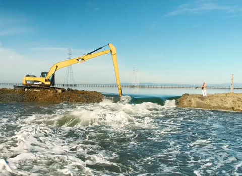 A bulldozer works to remove part of an earthen levy separating two bodies of water.