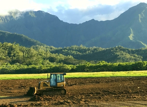 A dozer levels brown earth. Behind it are dramatic green mountains.