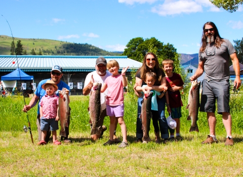 A group of adults with children show off the large trout they have just caught on a sunny June day.