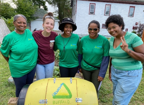 5 people stand with arms around each in front of a yellow barrel-shaped object with the words "groundwork Buffalo" written on it