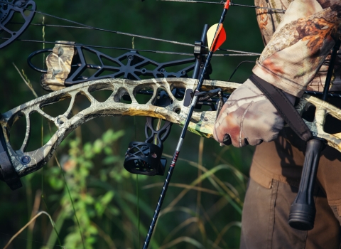 Arm of hunter in camo holding a bow.