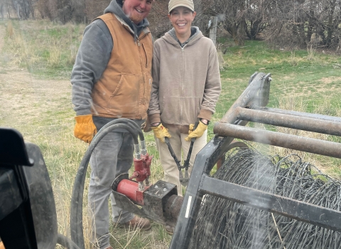 A man an a woman are smiling behind a large coil of fence.