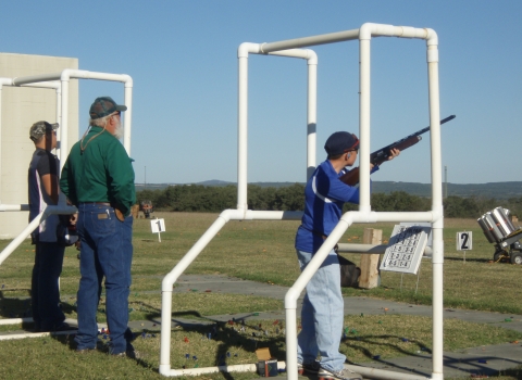 Boy aims sporting rifle at targets while standing behind a mobile range stand. 