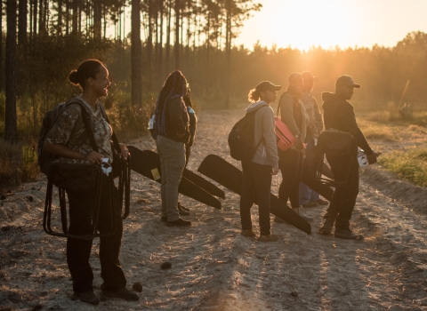 Fort Valley State University students, dressed for hunting, stand on dirt road at sunrise. 