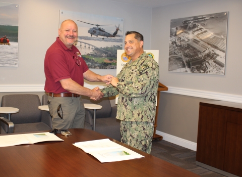 two men shake hands while standing behind large table