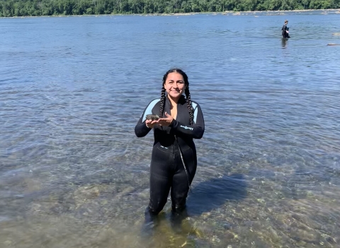 Intern in river holding a freshwater mussel