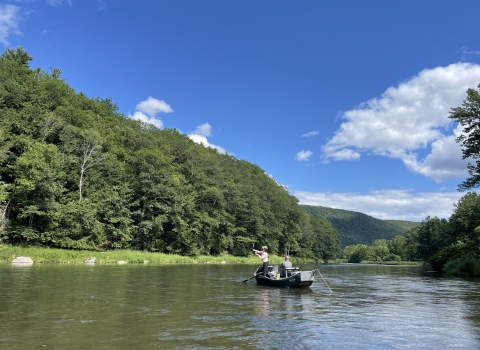 2 people in a boat on a waterbody surrounded by trees with a mountain in the background