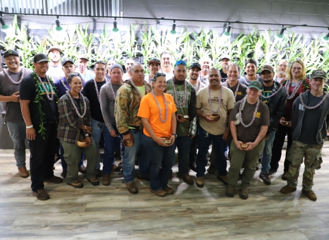 Awardees from the USFWS ceremony on Maui gather for a group photo in front of a plant wall of a dimly lit room. 