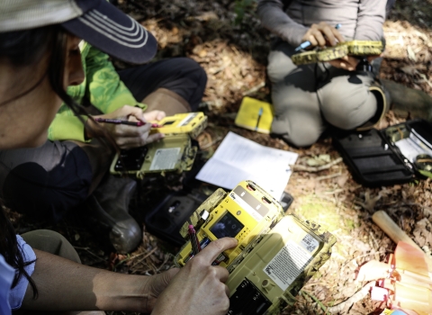 People sitting outdoors in a circle, holding an electronic device in their hands