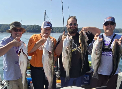 4 men holding striped bass on a boat