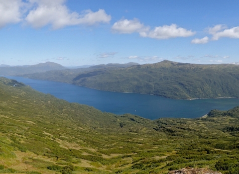 Cerulean blue water stretches between sloped mountains beneath a partly cloudy sky.