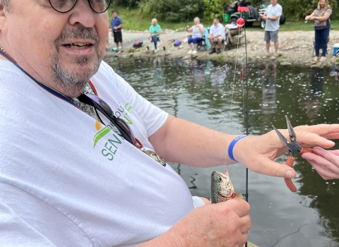 Man holding fish and fishing pole by stream