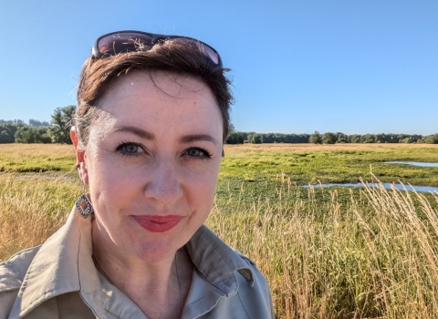 Smiling person with sunglasses on head stands in front of wetlands. 