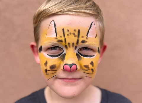 a blond child with their face painted to look like an ocelot