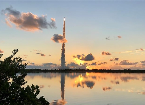 A rocket launches up to space in the golden dawn light from Cape Canaveral.