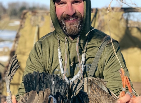 person wears a necklace of bands and holds ducks in hands