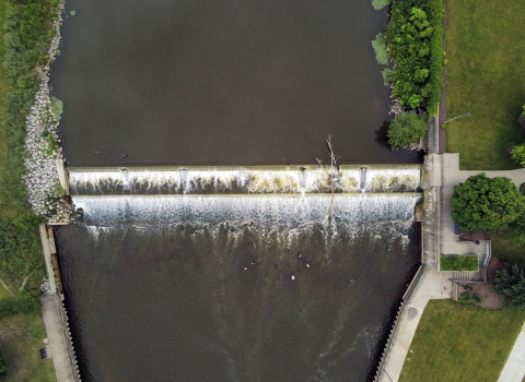 Aerial view of a dam in a dark river with green grass on both side