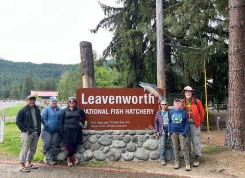 A group of six stands by the Leavenworth National Fish Hatchery entrance sign