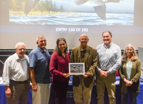 Six judges at the 2025 Federal Duck Stamp Art Contest hold the winning artwork.