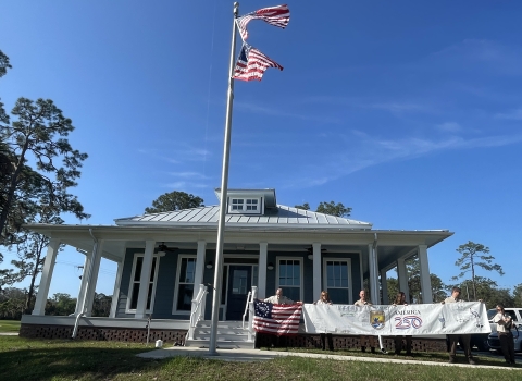 office building with 2 US flags on flagpole in front and people holding banner, Freedom 250 flag